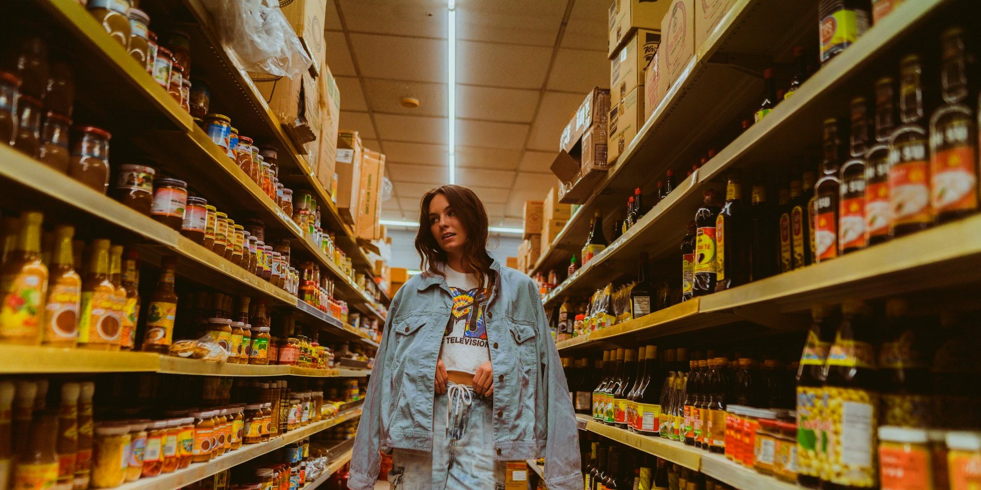 A shopper walking down a grocery aisle, shelves on both sides.