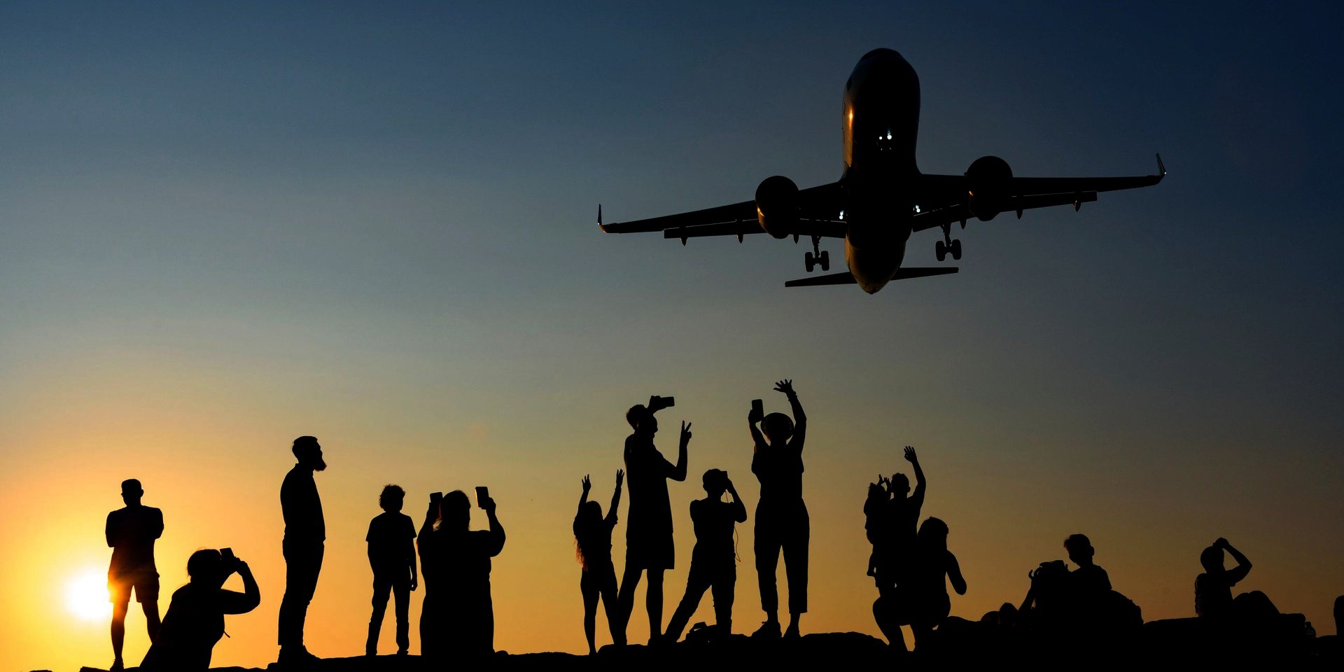 People silhouetted at sunset, watching a plane come in to land.